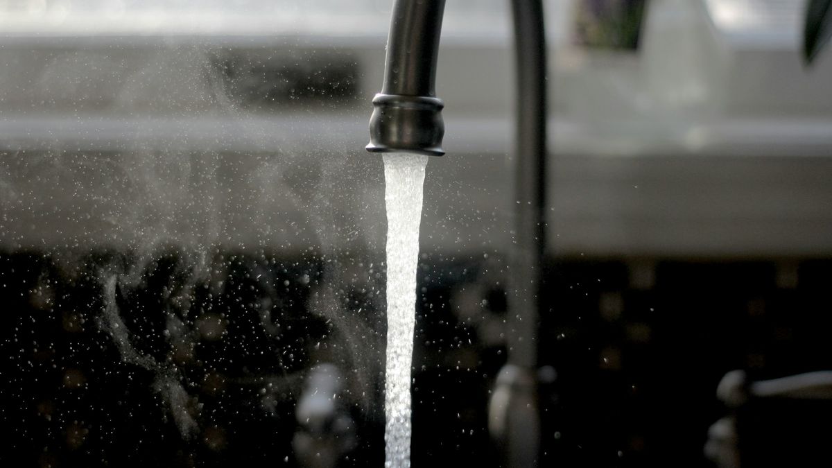 Torneira de cozinha moderna em preto fosco com água corrente saindo do bico, close-up