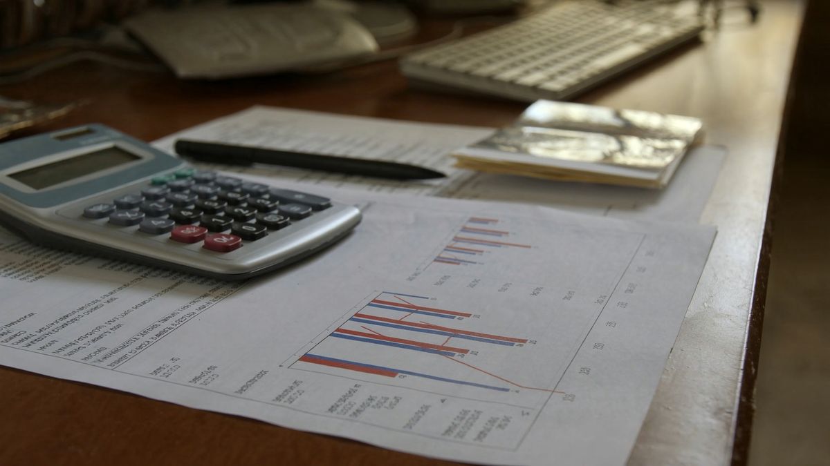 Síndico analisando planilha de orçamento e relatório financeiro do condomínio sobre uma mesa, com calculadora ao lado