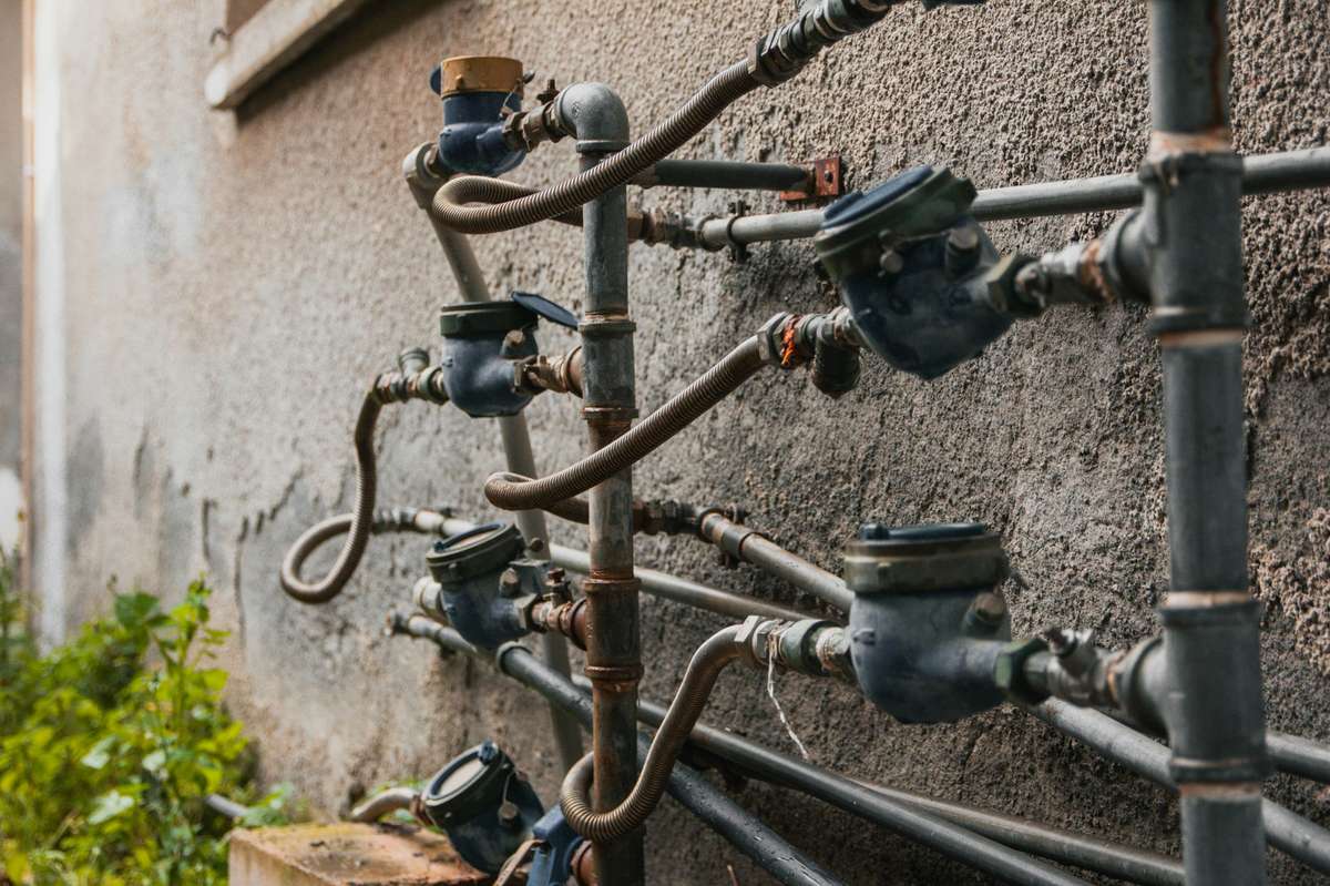 Vários hidrômetros individuais instalados lado a lado na parede externa de um prédio, conectados por tubulações metálicas