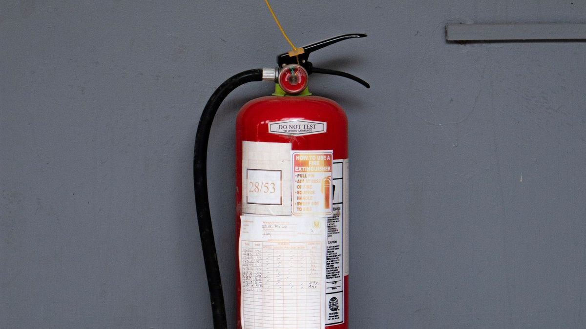 Extintor de incêndio vermelho fixado na parede de área comum de condomínio, com placa de sinalização ao lado